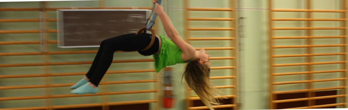 Ett barn gungar i romerska ringar framför ribbstolarna i en gympasal